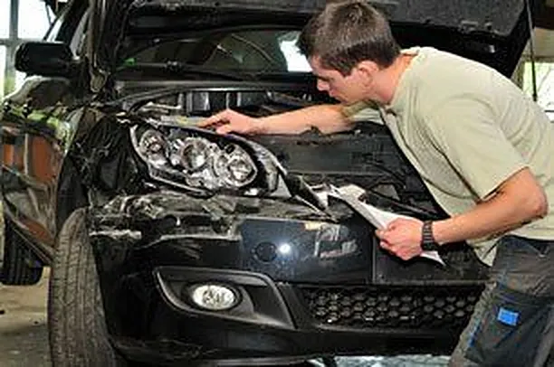 Technician inspecting a damaged front end with the hood open