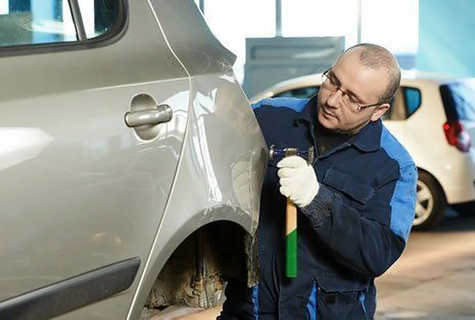 Technician working a dent out of a car's rear quarter panel with a hand tool