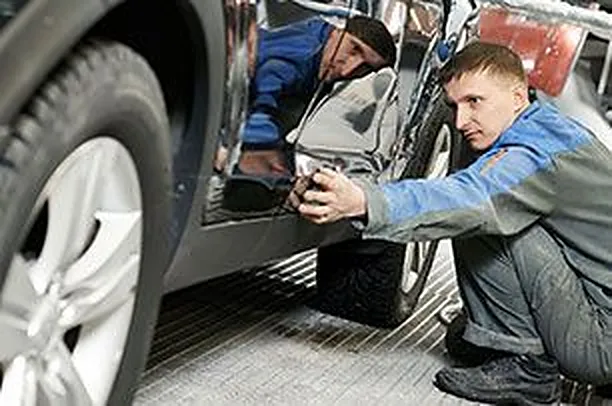 Two technicians working on the lower body and frame of a silver car